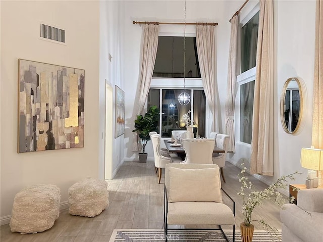 living area with a towering ceiling, baseboards, visible vents, and wood finished floors