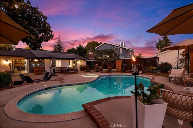 pool at dusk featuring a patio and an in ground hot tub