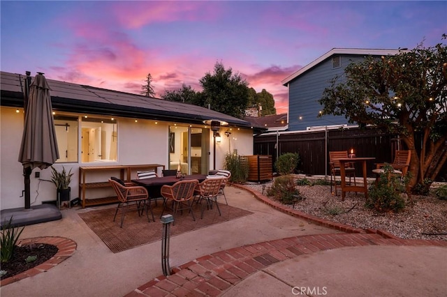 back house at dusk featuring a patio and solar panels