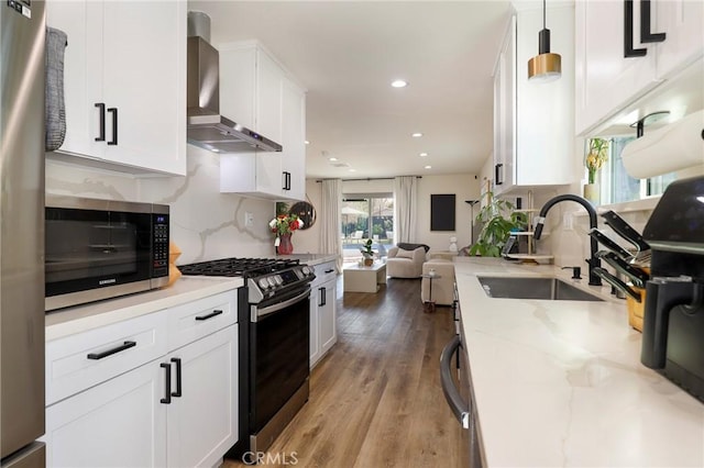 kitchen featuring wall chimney range hood, stainless steel appliances, white cabinets, and sink