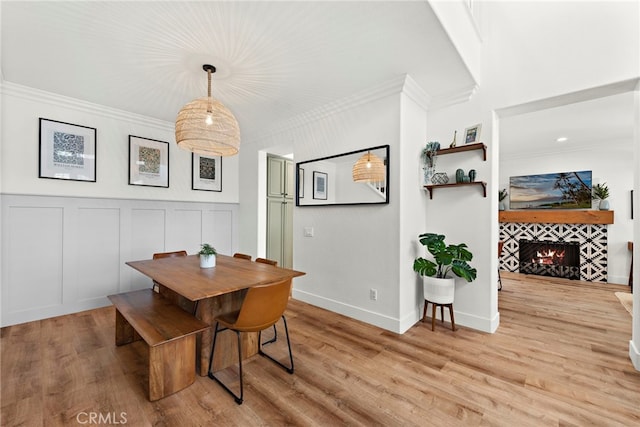 dining room with a tile fireplace, light wood-style flooring, a decorative wall, baseboards, and ornamental molding