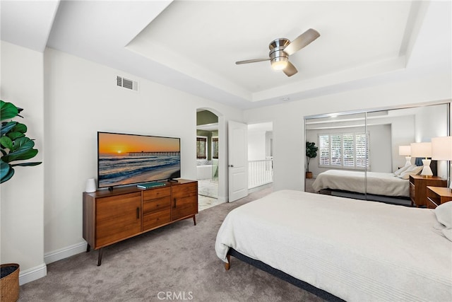 carpeted bedroom featuring arched walkways, a raised ceiling, visible vents, a ceiling fan, and baseboards