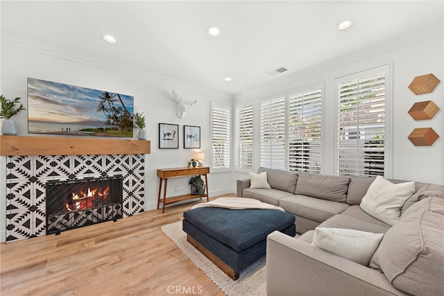 living room with recessed lighting, visible vents, a tiled fireplace, ornamental molding, and wood finished floors