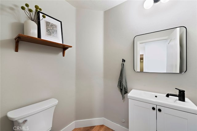 half bath with baseboards, vanity, toilet, and wood finished floors