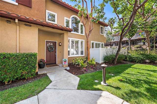 property entrance with a tile roof, fence, a lawn, and stucco siding