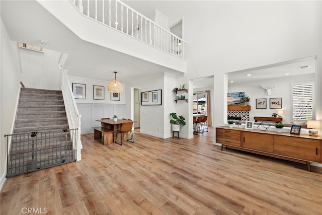 living room with crown molding, a towering ceiling, light wood-style floors, baseboards, and stairs