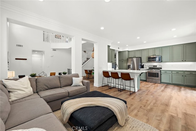 living room featuring light wood finished floors, stairway, visible vents, and crown molding