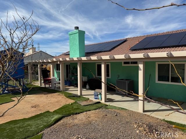 rear view of property featuring central AC unit, solar panels, stucco siding, a chimney, and a patio area