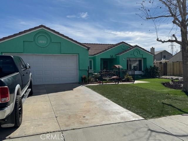 ranch-style house featuring a garage, a tile roof, driveway, stucco siding, and a front lawn