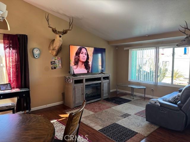 living room featuring lofted ceiling, dark wood-type flooring, a glass covered fireplace, and baseboards