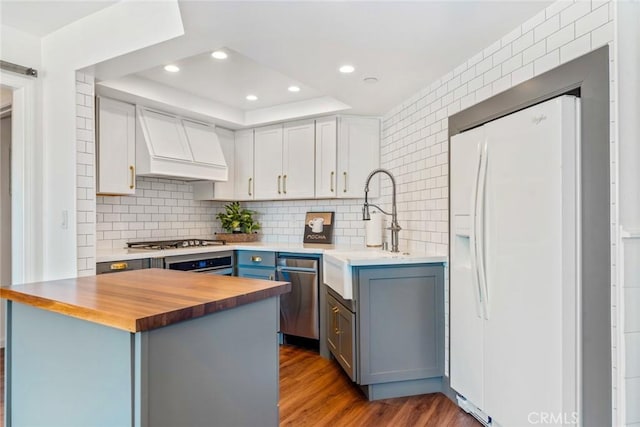 kitchen featuring stainless steel appliances, custom exhaust hood, wood counters, and decorative backsplash