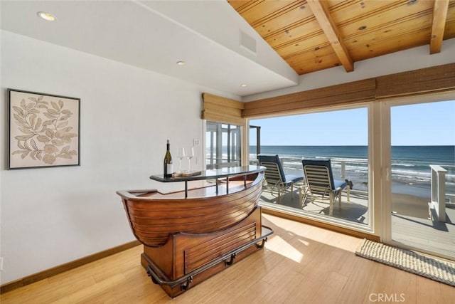 interior space with a water view, light hardwood / wood-style floors, wooden ceiling, vaulted ceiling with beams, and a beach view