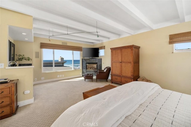 bedroom with beamed ceiling, light colored carpet, and a tiled fireplace