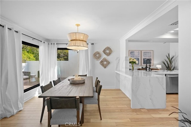 dining space with sink, crown molding, and light wood-type flooring