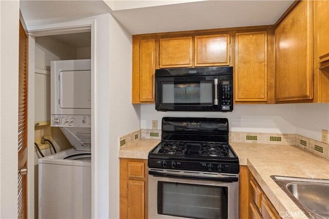 1150 E Palm Canyon Dr Unit 51, Palm Springs, CA 92264 - kitchen featuring black microwave, stainless steel gas range oven, stacked washer and clothes dryer, light countertops, and brown cabinets