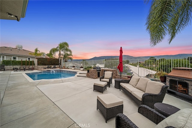 pool at dusk with a patio area, a mountain view, an outdoor living space with a fireplace, a fenced backyard, and a fenced in pool