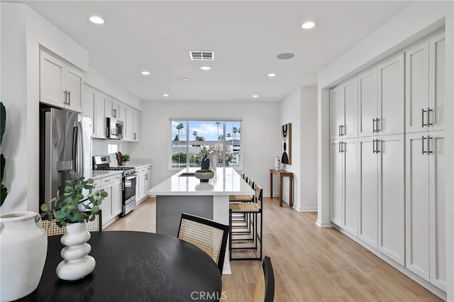 kitchen with light wood-type flooring, stainless steel appliances, a kitchen island, white cabinets, and a kitchen breakfast bar