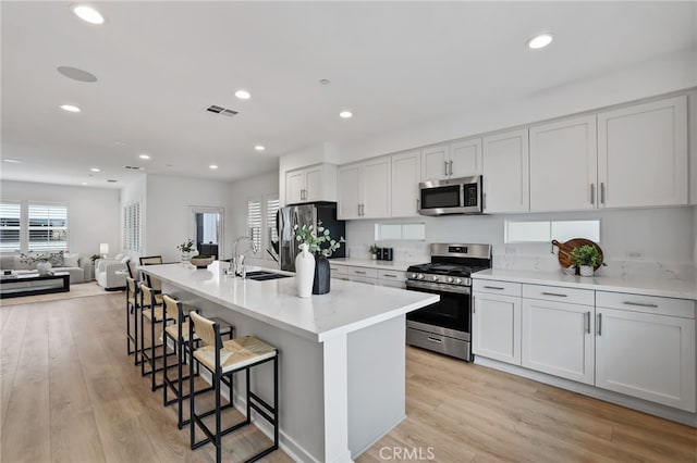 kitchen with appliances with stainless steel finishes, a kitchen bar, white cabinets, and a center island with sink