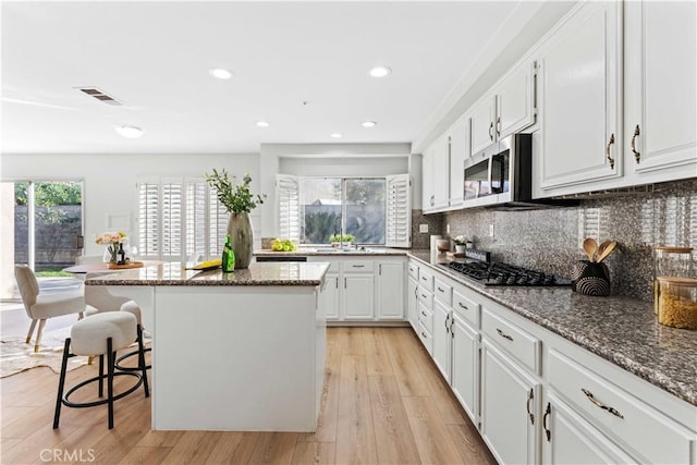 kitchen with white cabinetry, dark stone countertops, a center island, a breakfast bar, and appliances with stainless steel finishes