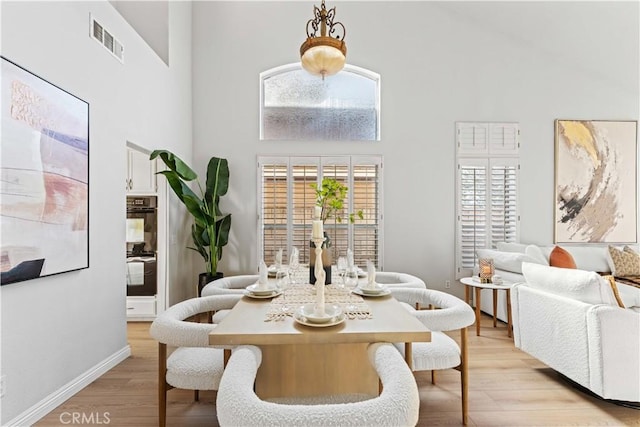 dining room featuring light wood-type flooring and a towering ceiling