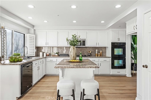 kitchen with light stone countertops, black appliances, a center island, light wood-type flooring, and white cabinetry