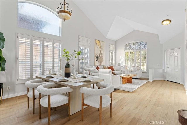 dining space with high vaulted ceiling and light hardwood / wood-style flooring