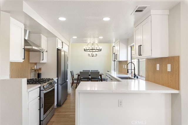 kitchen featuring sink, stainless steel appliances, wall chimney exhaust hood, kitchen peninsula, and white cabinets