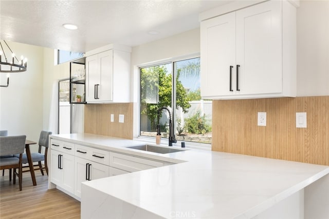 kitchen with tasteful backsplash, a notable chandelier, light hardwood / wood-style floors, sink, and white cabinetry