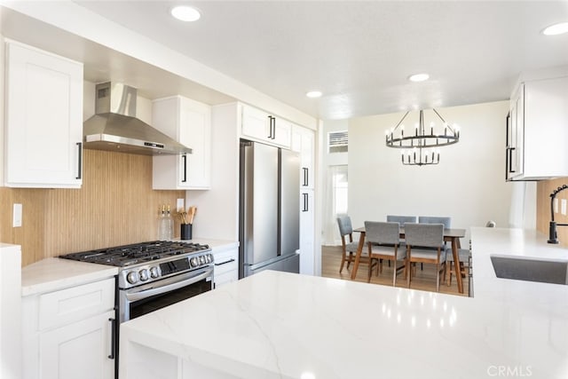 kitchen with appliances with stainless steel finishes, sink, light stone counters, white cabinetry, and wall chimney range hood