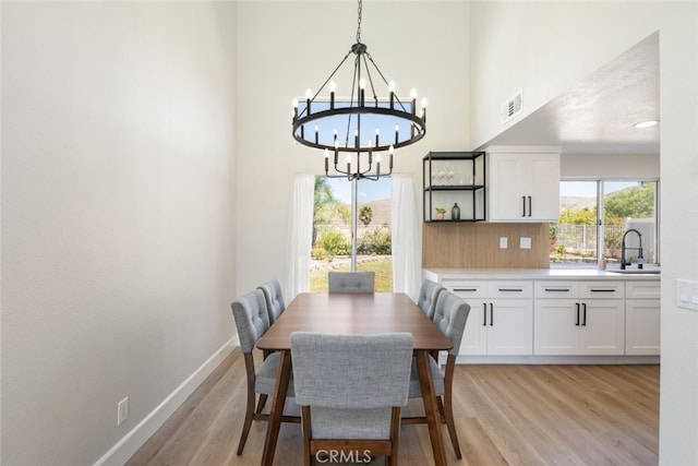 dining space with sink, light hardwood / wood-style floors, a high ceiling, and a notable chandelier