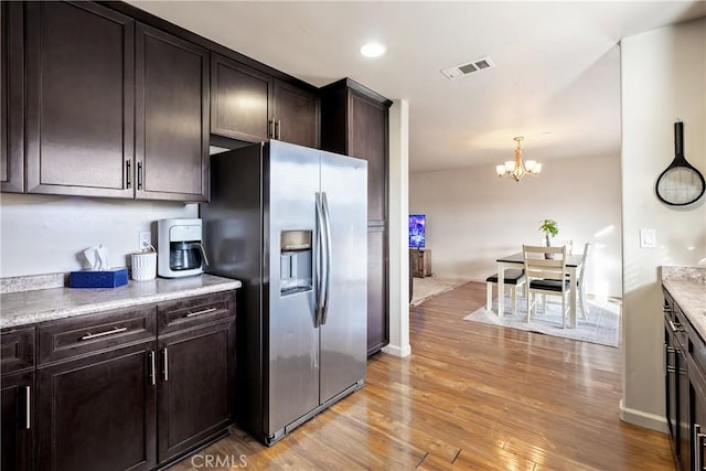 kitchen with dark brown cabinetry, light stone countertops, stainless steel refrigerator with ice dispenser, light hardwood / wood-style floors, and pendant lighting