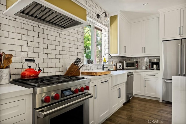 kitchen featuring premium appliances, white cabinets, sink, and wall chimney range hood