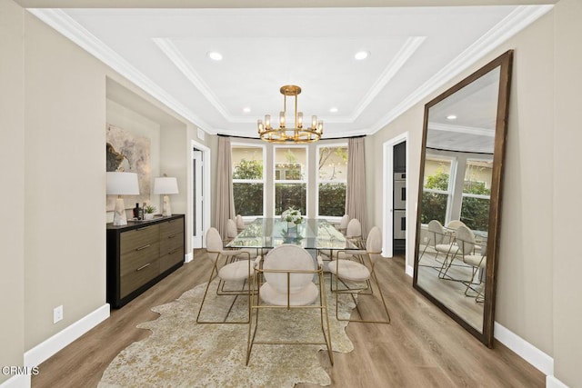 dining space with a raised ceiling, light hardwood / wood-style floors, crown molding, and a notable chandelier