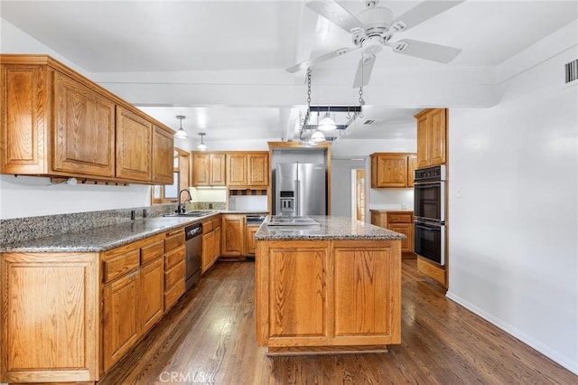 kitchen with appliances with stainless steel finishes, decorative light fixtures, a kitchen island, dark hardwood / wood-style floors, and dark stone countertops