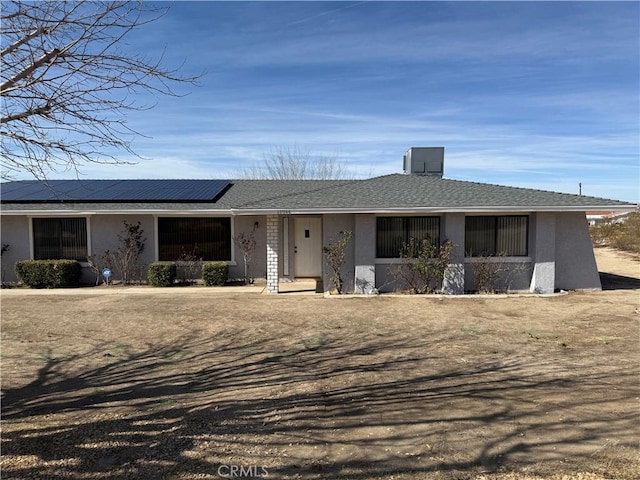 ranch-style home with solar panels, roof with shingles, and stucco siding