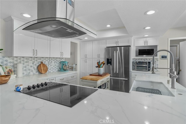 kitchen with black electric stovetop, stainless steel fridge with ice dispenser, island range hood, white cabinetry, and a sink