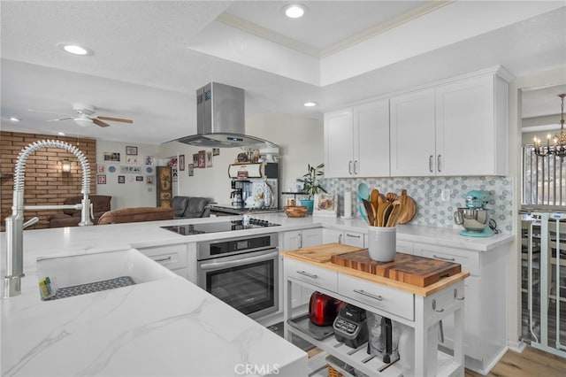 kitchen featuring tasteful backsplash, stainless steel oven, black electric cooktop, island range hood, and white cabinetry