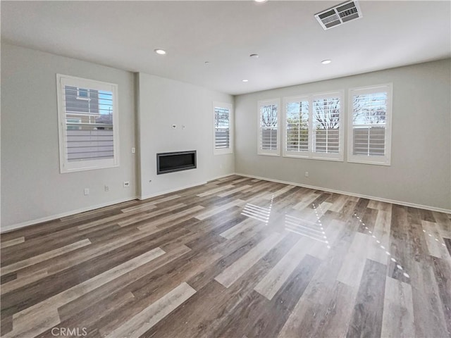 unfurnished living room featuring recessed lighting, wood finished floors, visible vents, baseboards, and a glass covered fireplace