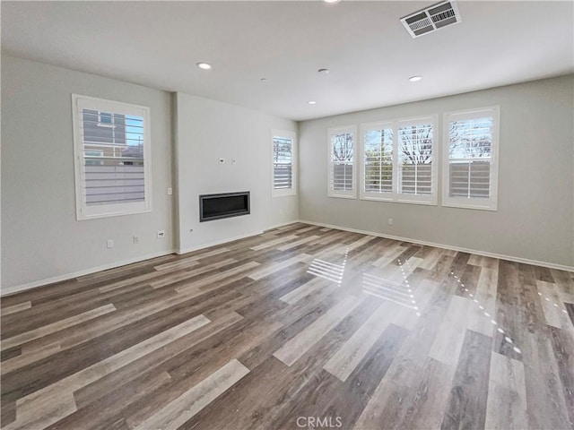 unfurnished living room featuring baseboards, visible vents, a glass covered fireplace, wood finished floors, and recessed lighting