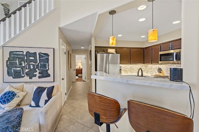 kitchen with light tile patterned floors, backsplash, pendant lighting, stainless steel appliances, and dark brown cabinetry