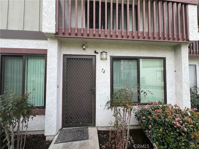 view of exterior entry with a balcony and stucco siding