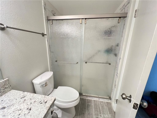 bathroom with a stall shower, wood finish floors, a textured wall, and toilet