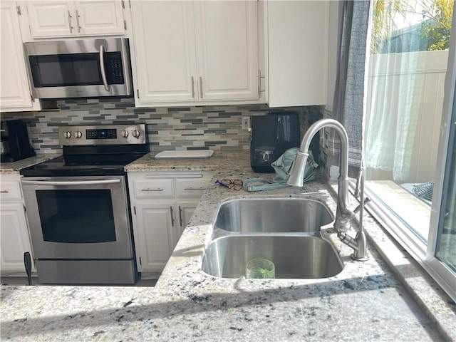 kitchen with stainless steel appliances, backsplash, white cabinets, a sink, and light stone countertops