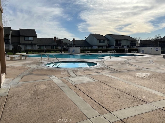 pool with a patio, fence, a residential view, and a hot tub