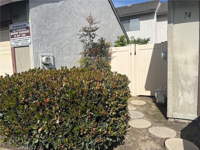 view of home's exterior with a shingled roof, a gate, fence, and stucco siding