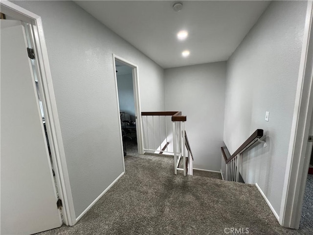 corridor with dark colored carpet, baseboards, and an upstairs landing