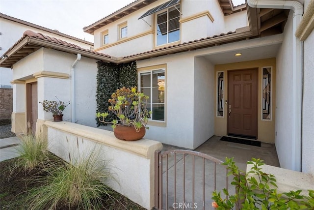 view of exterior entry with a tile roof, a gate, and stucco siding