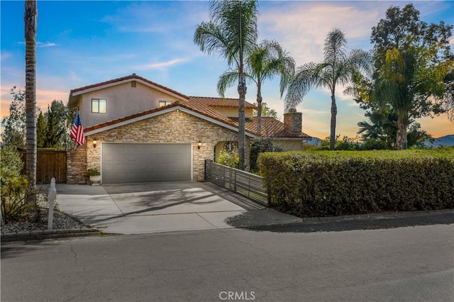 mediterranean / spanish-style house featuring a garage, stone siding, fence, and concrete driveway