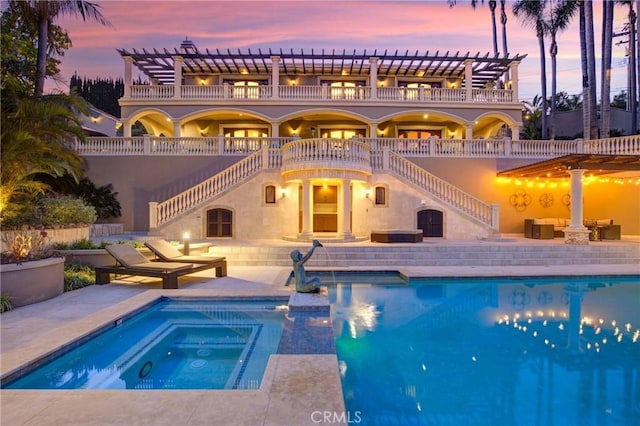 back of property at dusk featuring an outdoor pool, an in ground hot tub, a patio area, and a pergola