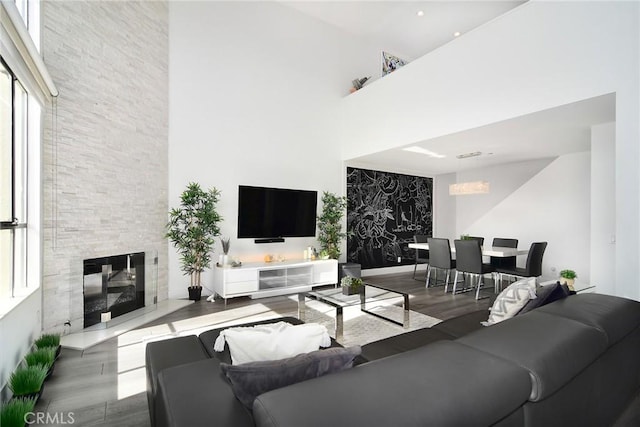 living room featuring a fireplace, a towering ceiling, wood-type flooring, and a wealth of natural light